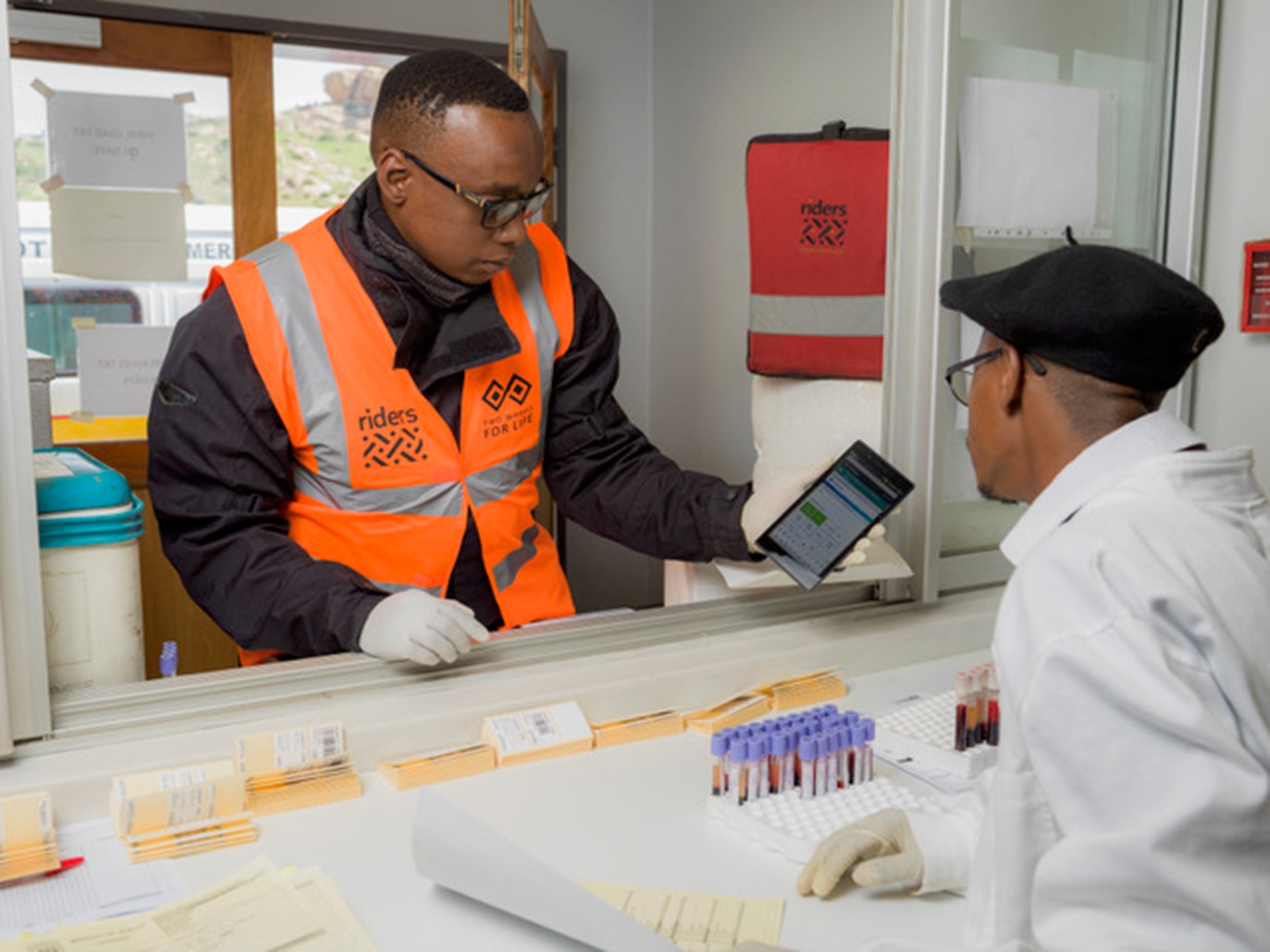 man shows mobile to scientist across a counter with vials of blood
