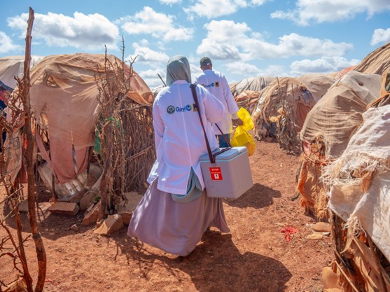 women in GAVI coats and long dresses walking through refugee settlement