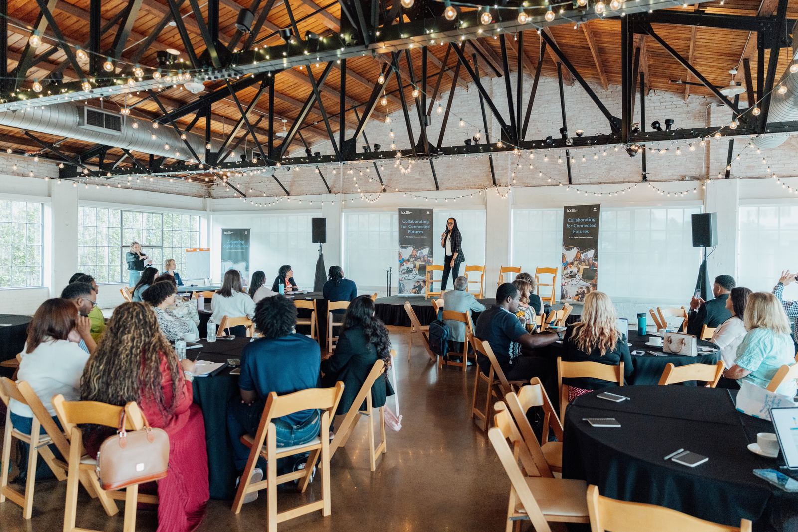 Attendees at a Collaborating for Connected Futures session in a string-lit venue with TCS Digital Empowers banners