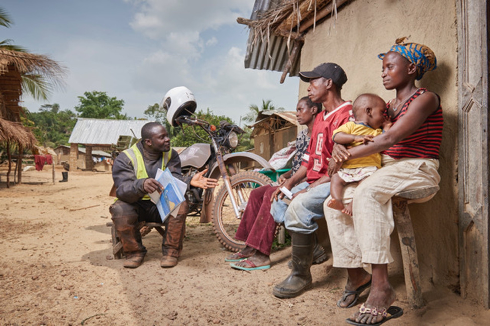 Global health rider explaining something to watching persons against a hut